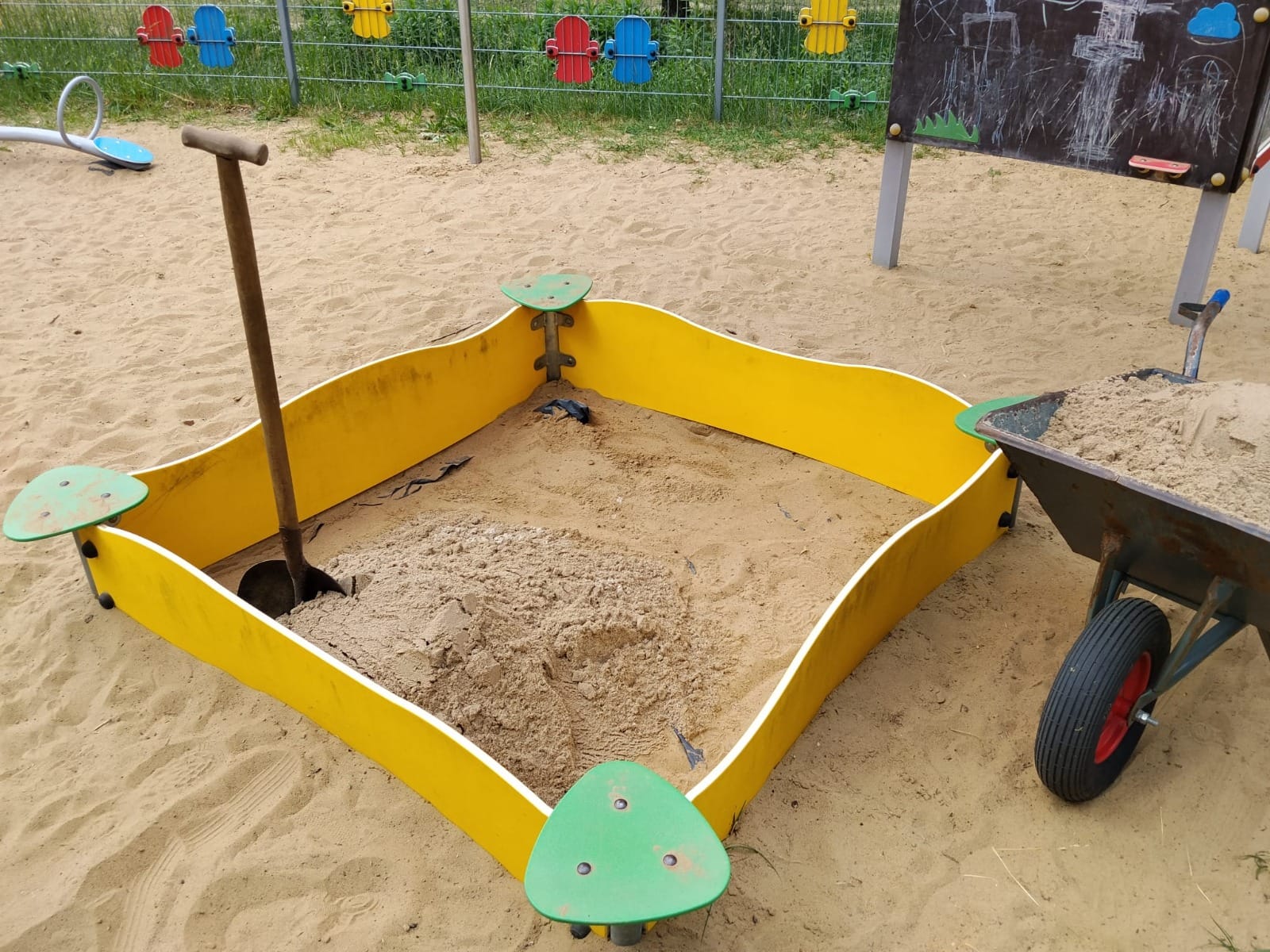 Piaskownica w trakcie wymiany — stary piasek wybrany, wbita łopata i taczka